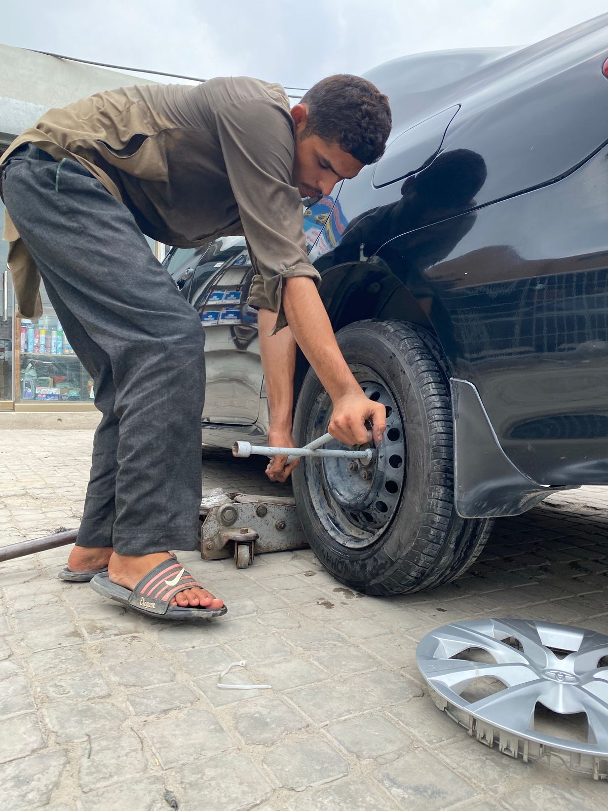 Person using a cross lug wrench to loosen lug nuts on a car tire before jacking up the vehicle