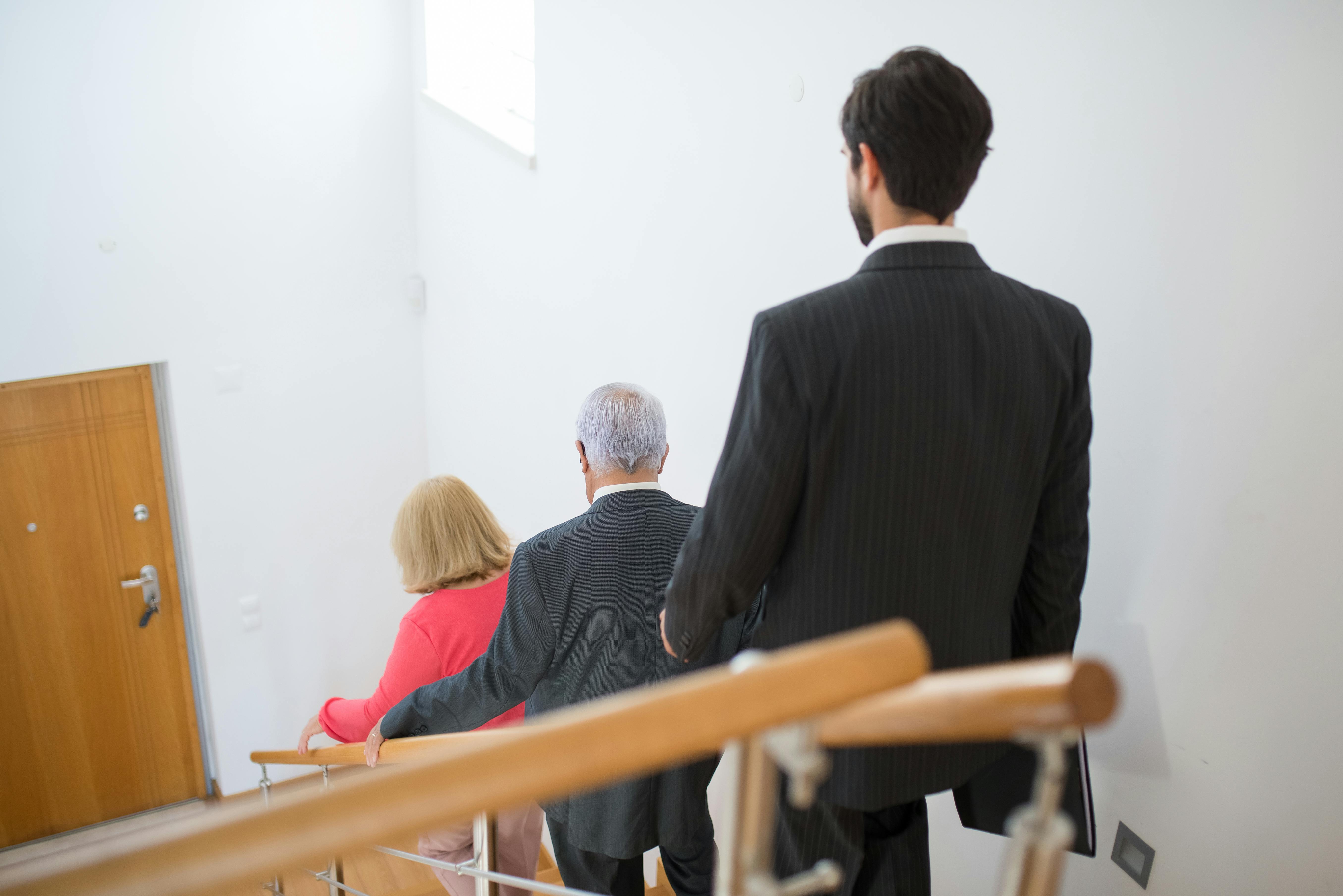 A senior couple and a young man in suits walking down a modern indoor staircase.