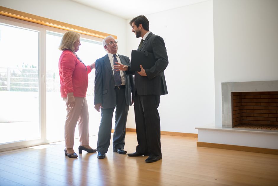 Älteres Ehepaar im Gespräch mit einem Immobilienmakler in einem leeren Wohnzimmer