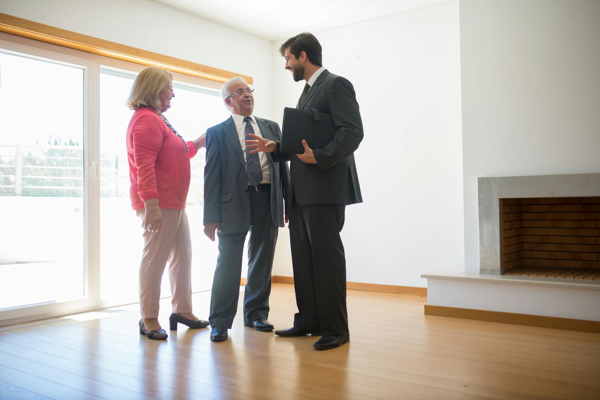 A real estate agent shows an empty house to senior clients, highlighting the spacious room.