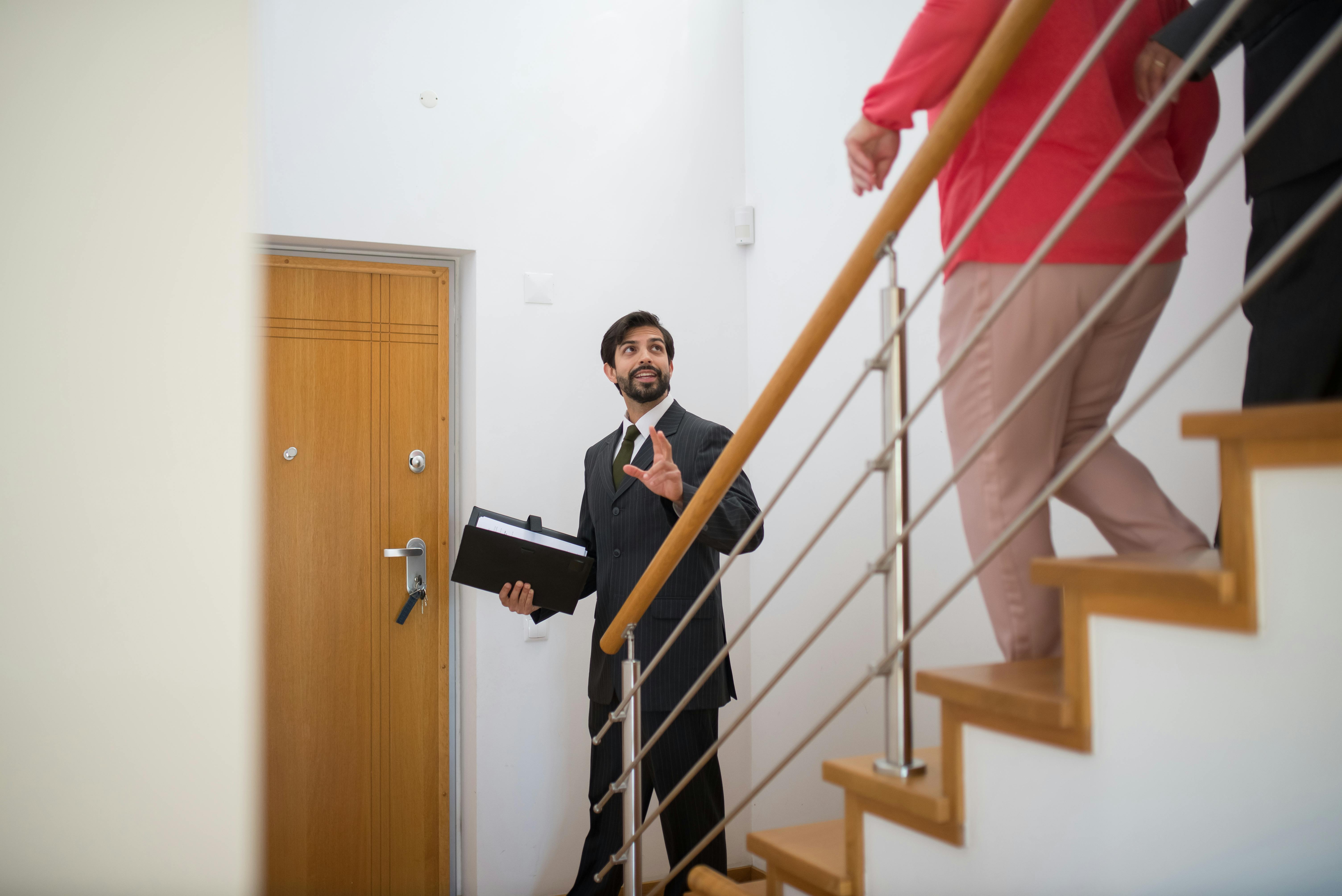 A realtor conducting a house tour with potential buyers on the stairs of a modern home.