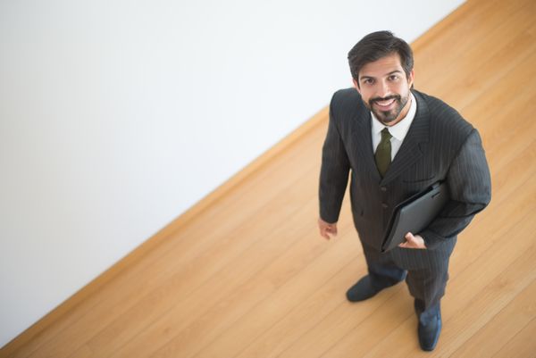Professional man in a suit smiling and holding a laptop, looking up.