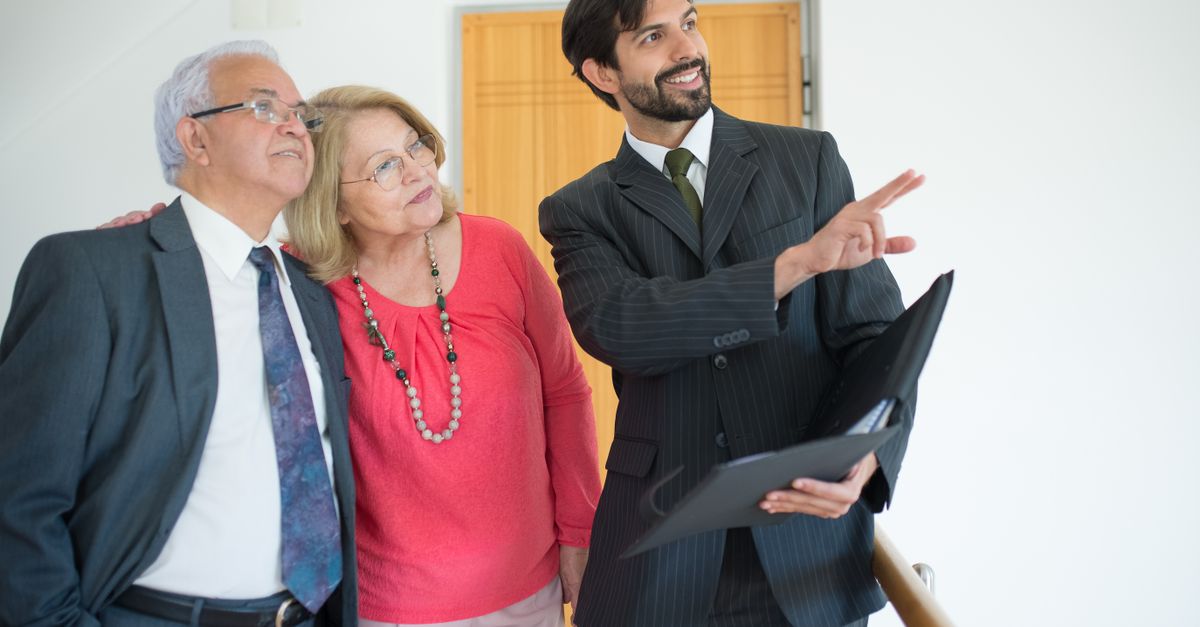 An elderly couple viewing a property with a realtor indoors, discussing real estate options.