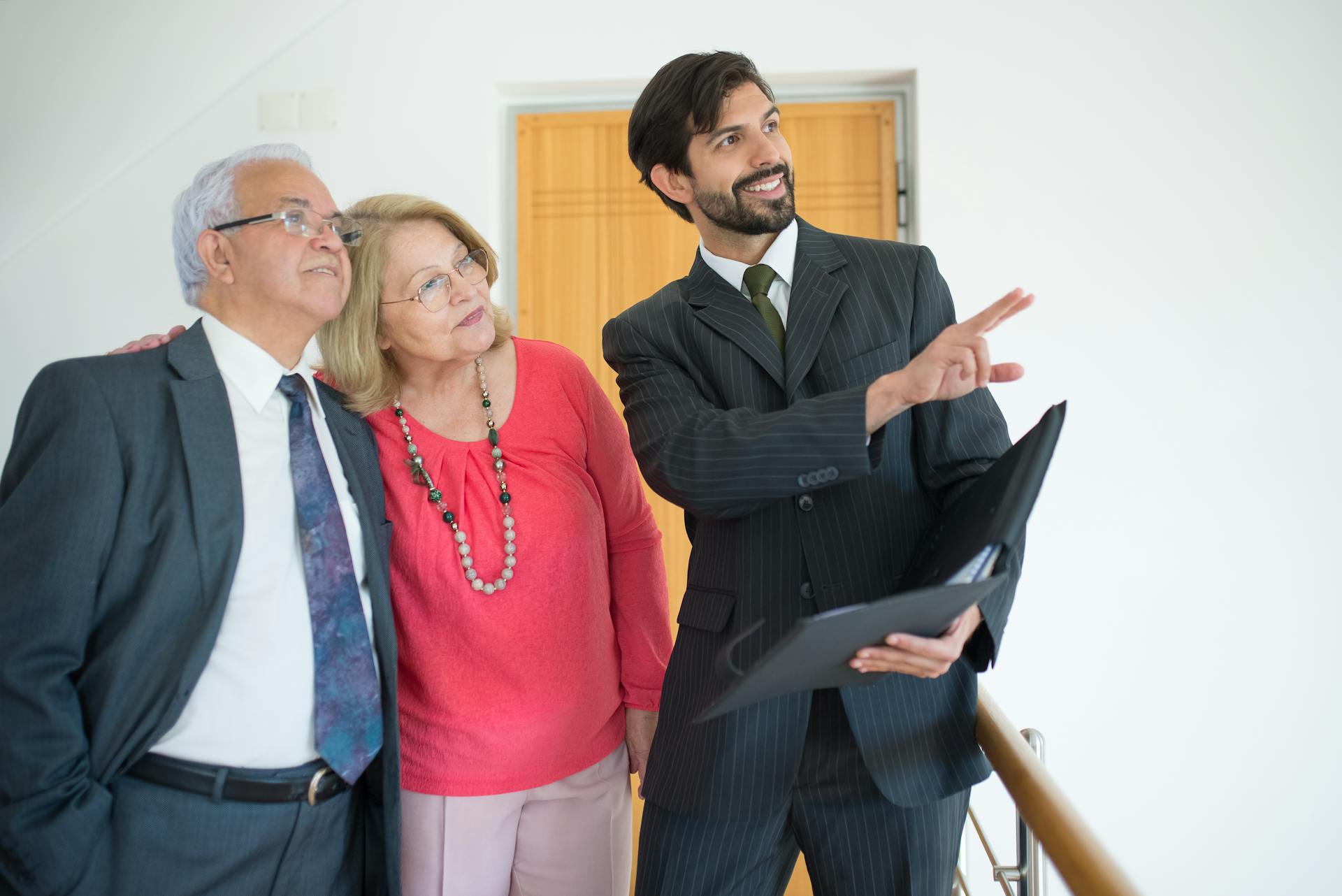 An elderly couple viewing a property with a realtor indoors, discussing real estate options.