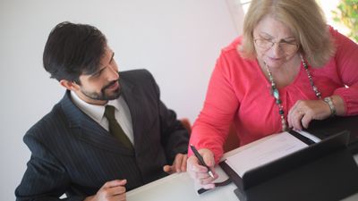 Abogado y mujer mayor sentados a la mesa, firmando un documento en una oficina luminosa, sobre albacea testamento Chile