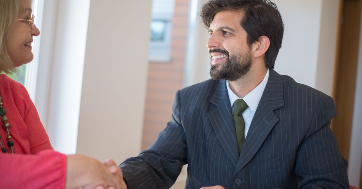 Professional real estate agent sealing a deal with a senior client indoors through a handshake.
