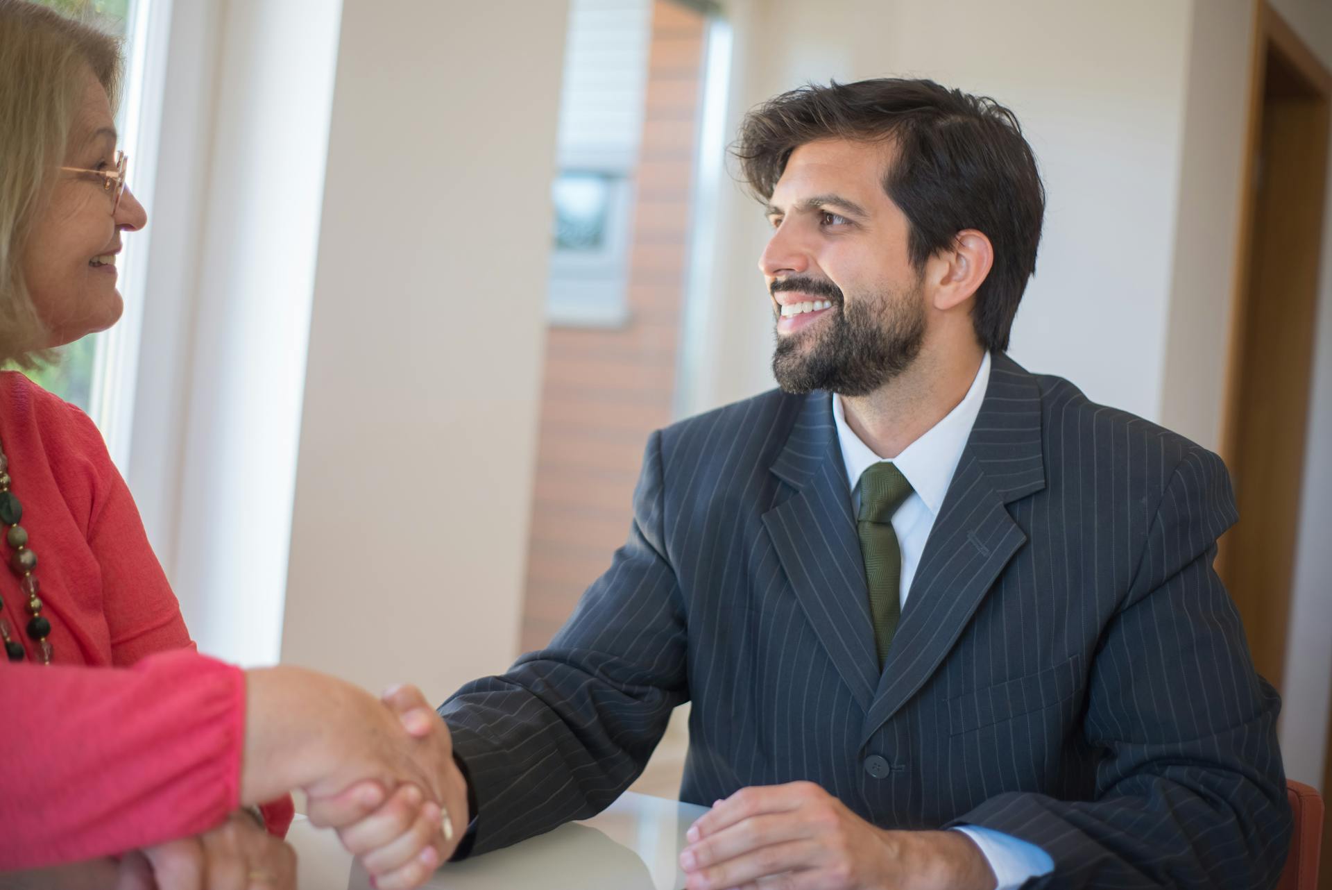 Professional real estate agent sealing a deal with a senior client indoors through a handshake.