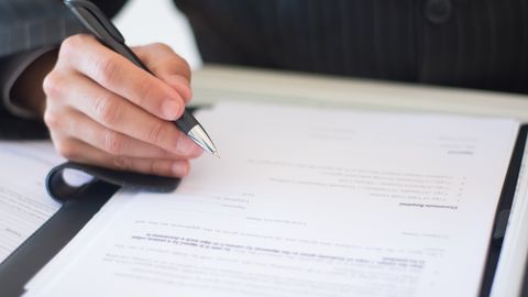 Close-up of a business professional signing documents in an office setting.
