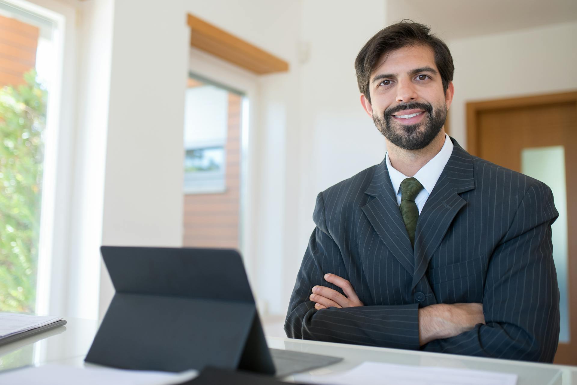 Professional businessman smiling in office with tablet, dressed in suit and tie.