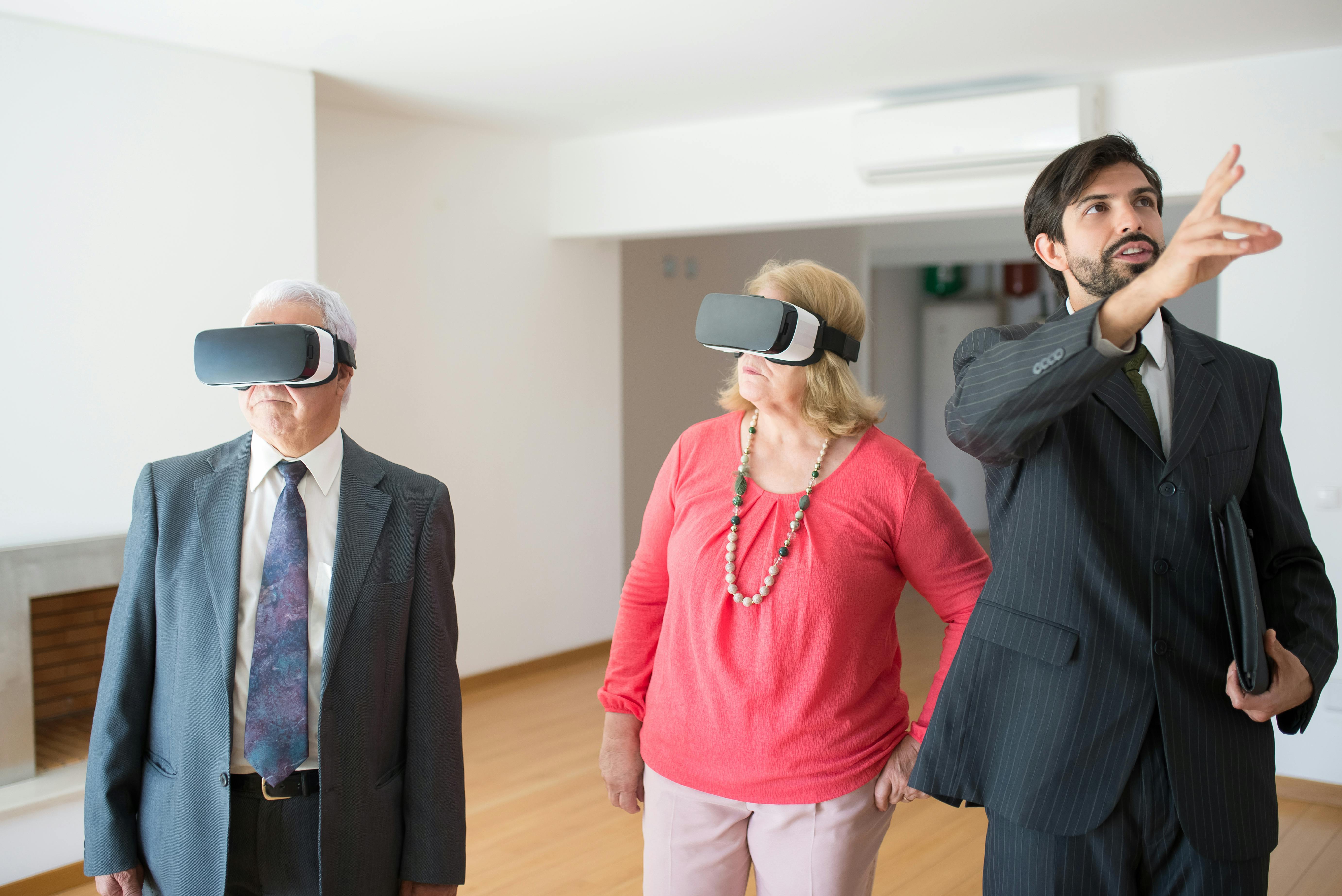 Senior couple using VR headsets in a modern apartment guided by a real estate agent.