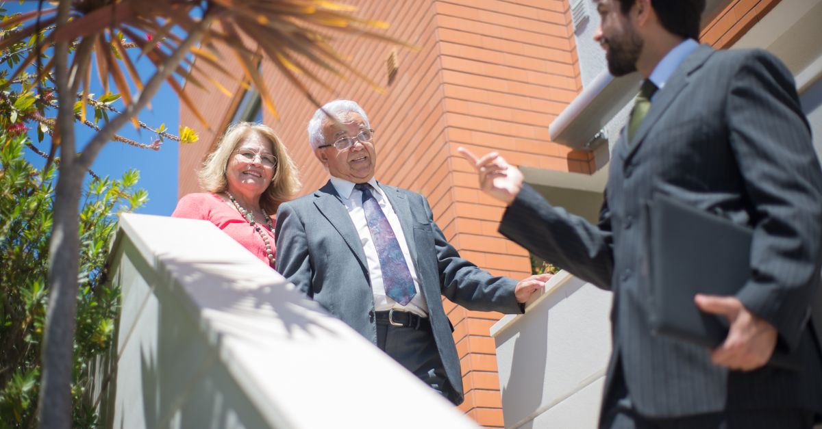 Elderly couple touring a modern home with a real estate agent in sunny Portugal.