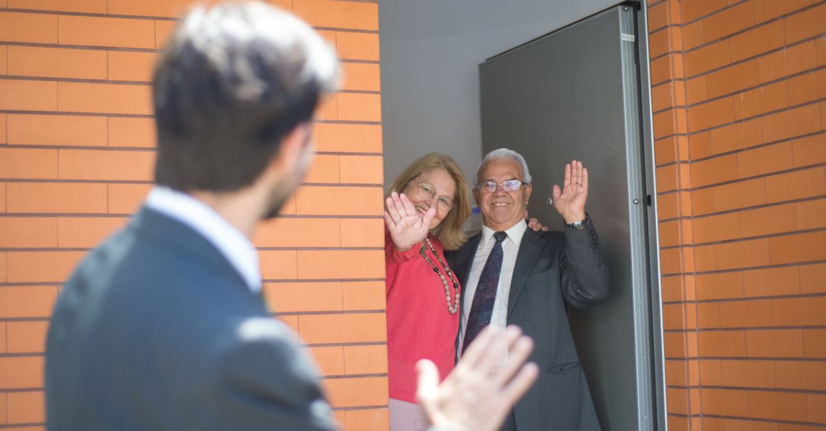 A happy couple waving goodbye from their doorway