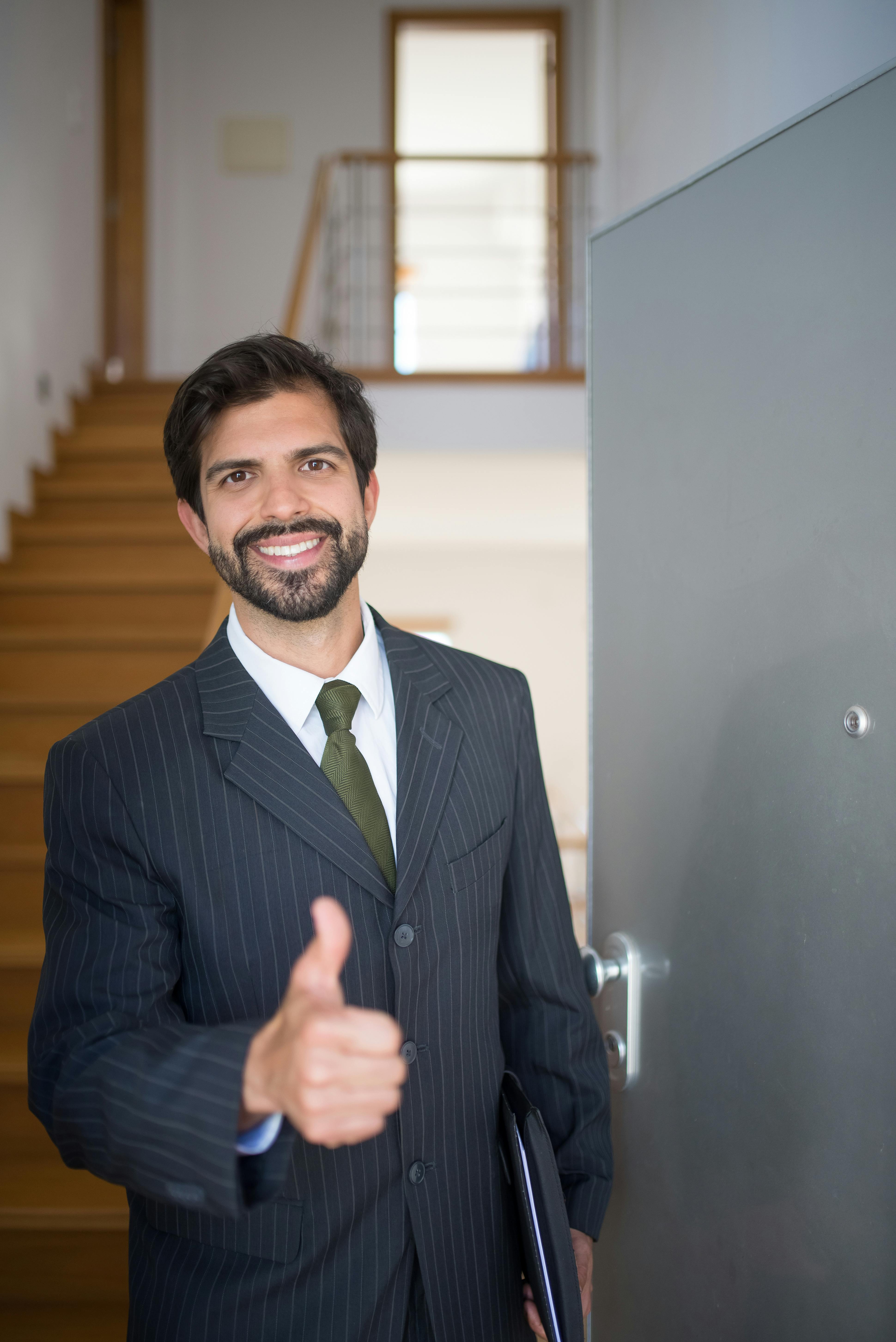 Smiling realtor giving thumbs up at open house indoors. Ideal for real estate marketing.