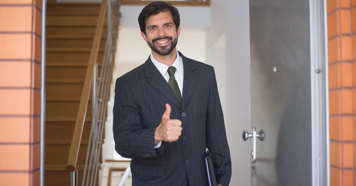 Smiling realtor gives a thumbs up at a modern open house entrance.