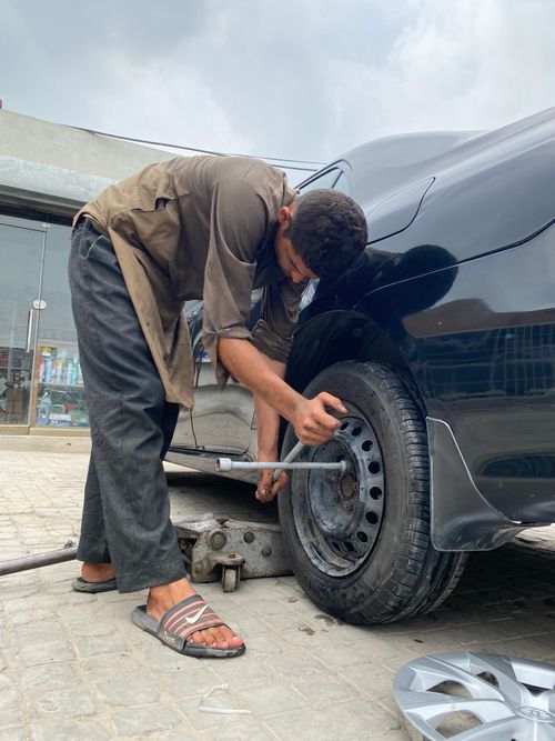 Free Young man repairing car wheel outdoors, showcasing automotive skills. Stock Photo