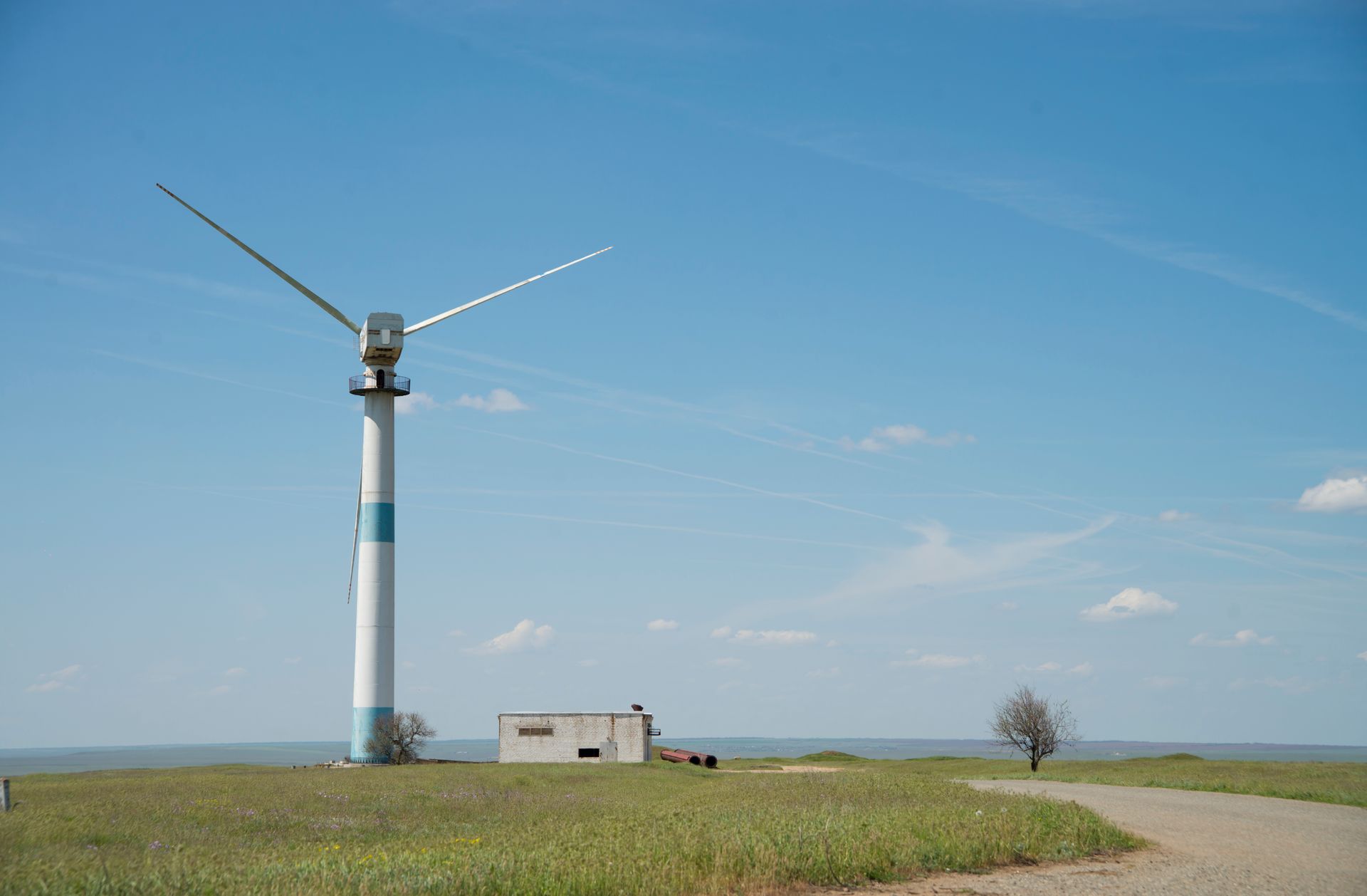 A solitary wind turbine stands amidst a grassland in Kalmykia, Russia, under a clear blue sky.