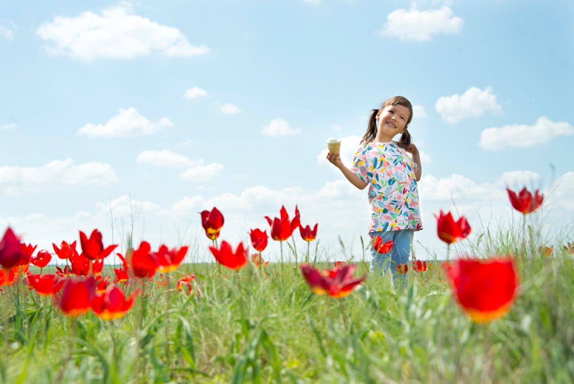 A Cute Girl in Floral Printed Shirt Standing on a Flower Field Holding an Ice Cream
