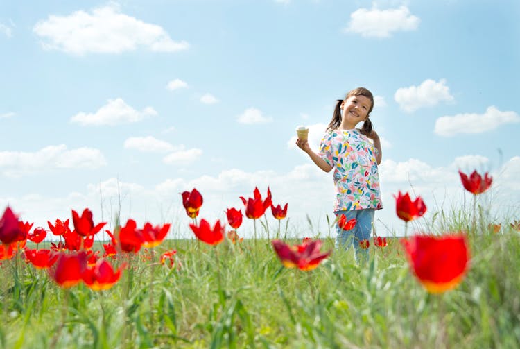 A Cute Girl In Floral Printed Shirt Standing On A Flower Field Holding An Ice Cream
