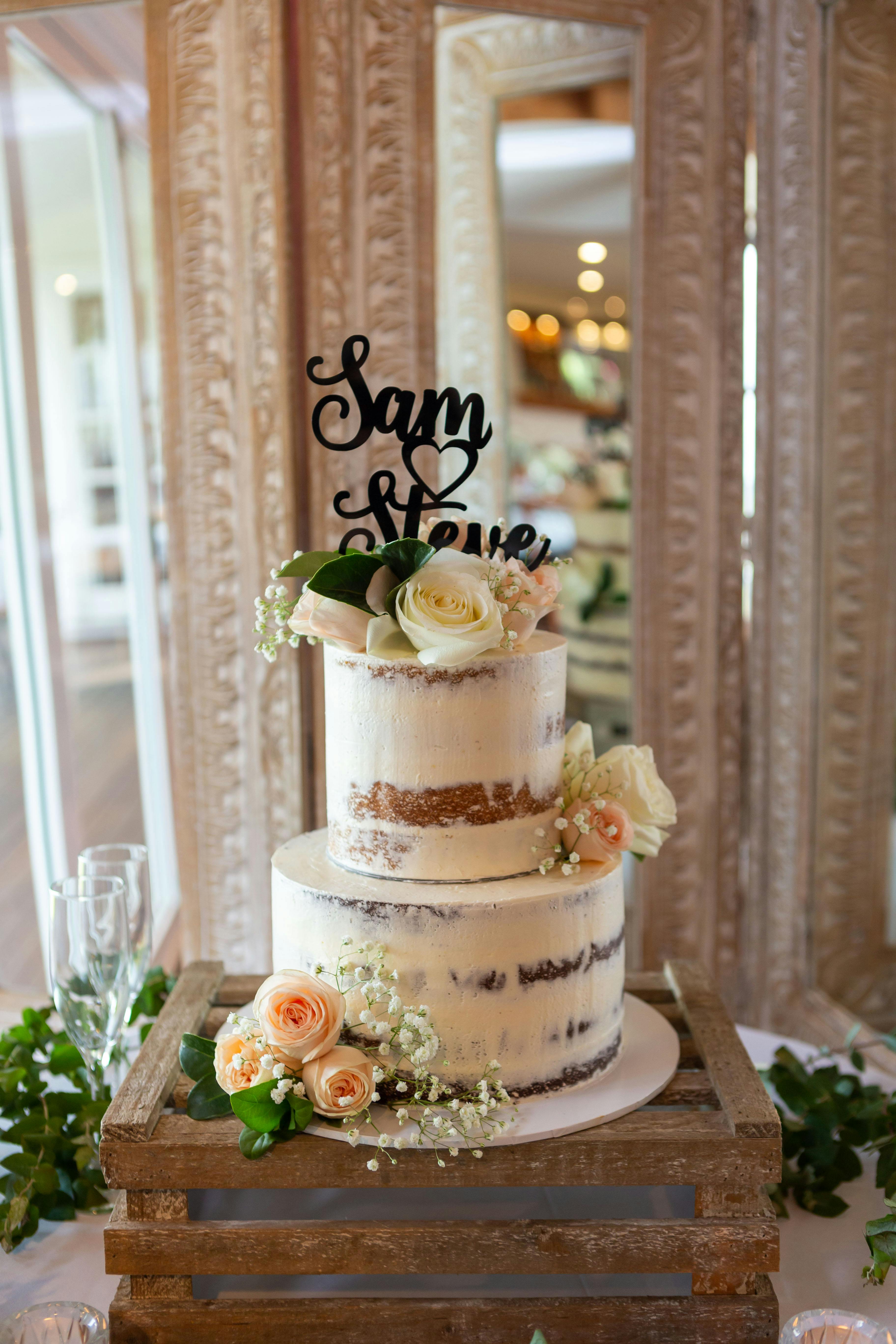 Charming semi-naked wedding cake adorned with roses and greenery, ideal for romantic celebrations.