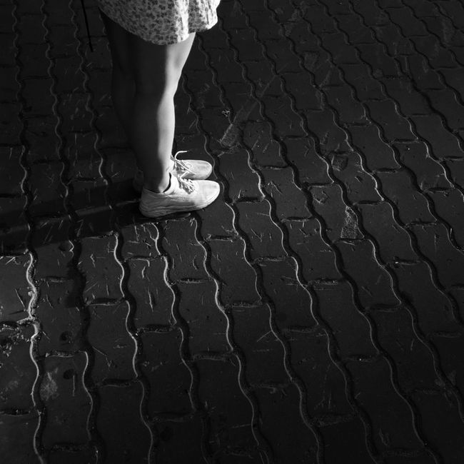 A stylish black and white photo capturing legs on a cobblestone path, highlighting fashion and texture.