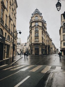 A striking baroque building stands at a corner in a European city on a wet day, framed by lampposts.