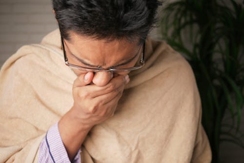 Close-Up Photo of a Sick Man Covering His Mouth