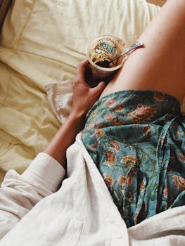 Enjoying a relaxed morning in bed with a cup of yogurt, wrapped in cozy attire.