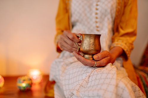 Free Close-up of hands holding a brass cup during a Diwali celebration with decorative candles. Stock Photo