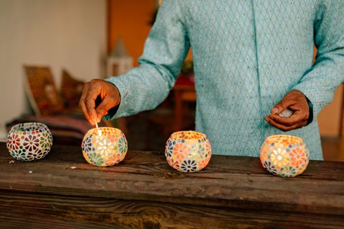 Free A person lights colorful mosaic candles, creating a warm festive atmosphere indoors. Stock Photo