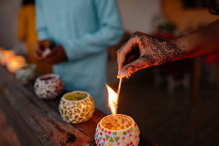 A Hand Lighting A Candle On Brown Wooden Surface
