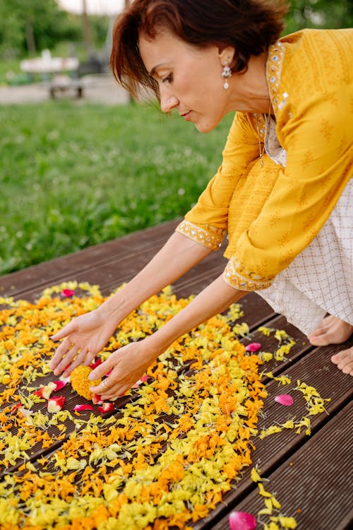 Free Woman in Yellow Dress Shirt and Blue Denim Jeans Holding Yellow and Red Flower Petals on on on on on Stock Photo