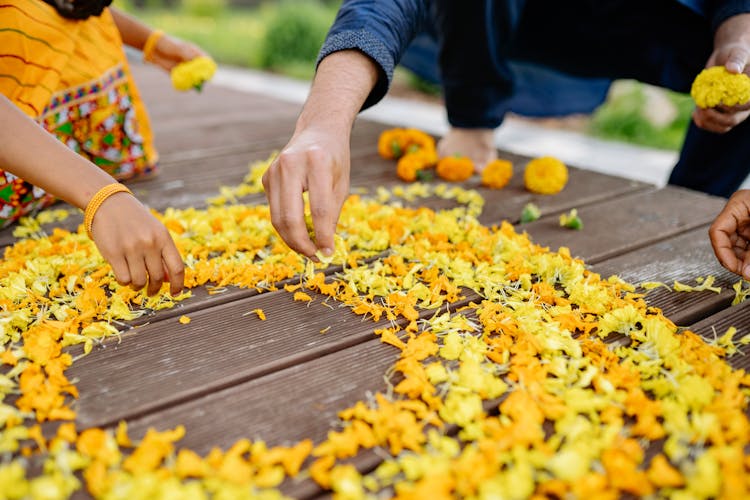 People Holding Yellow Petals On Brown Wooden Floor