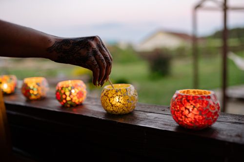 Free A henna-tattooed hand lighting colorful glass candles on a wooden surface at twilight. Stock Photo