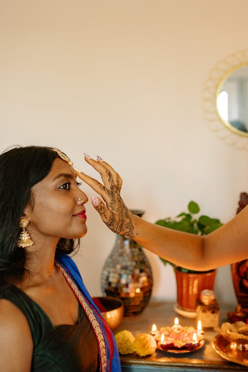 A Hand with Tattoo Putting Bindi on Woman's Forehead