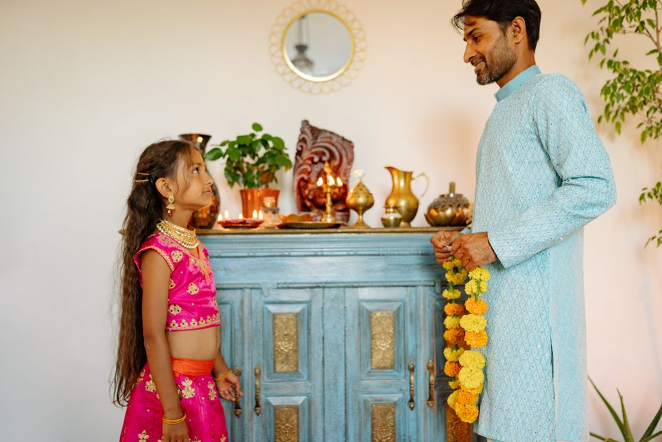 Man and girl in traditional clothing celebrating Diwali with flower garlands indoors.