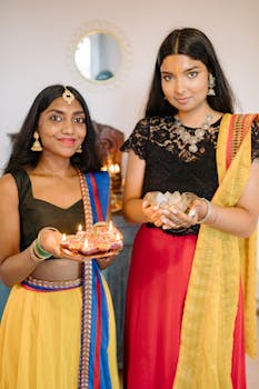 Two women in traditional Indian attire celebrating Diwali indoors with lit candles.
