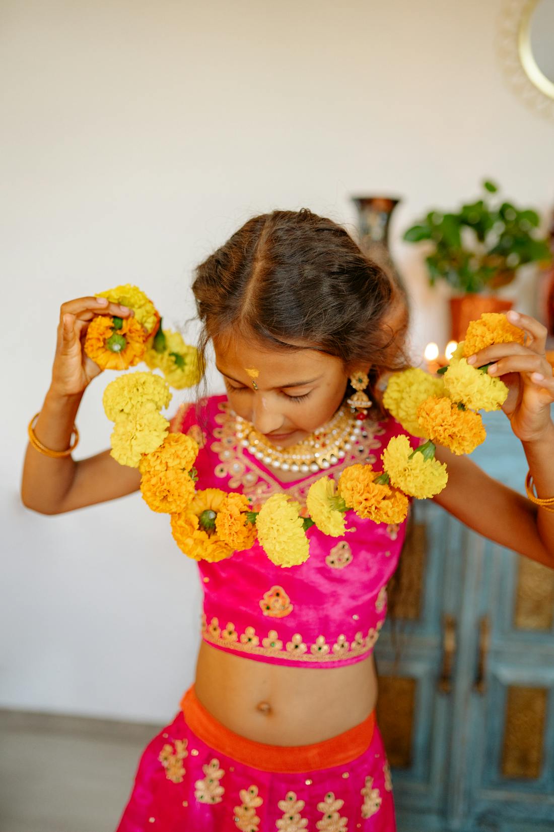Young girl adjusting a floral garland while wearing a bright orange lehenga