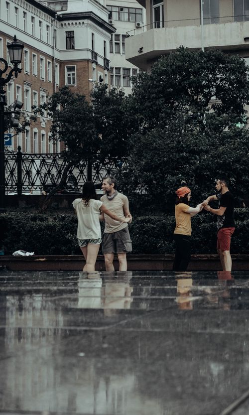 Free Group of adults dancing on a rainy street with buildings in the background. Stock Photo
