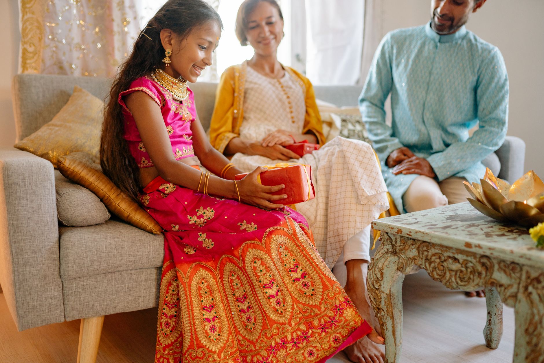 Smiling family celebrating Diwali with a child receiving a gift in traditional Indian clothing indoors.
