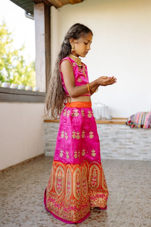 Free A young girl in a vibrant pink saree stands indoors, praying with joined hands. Stock Photo