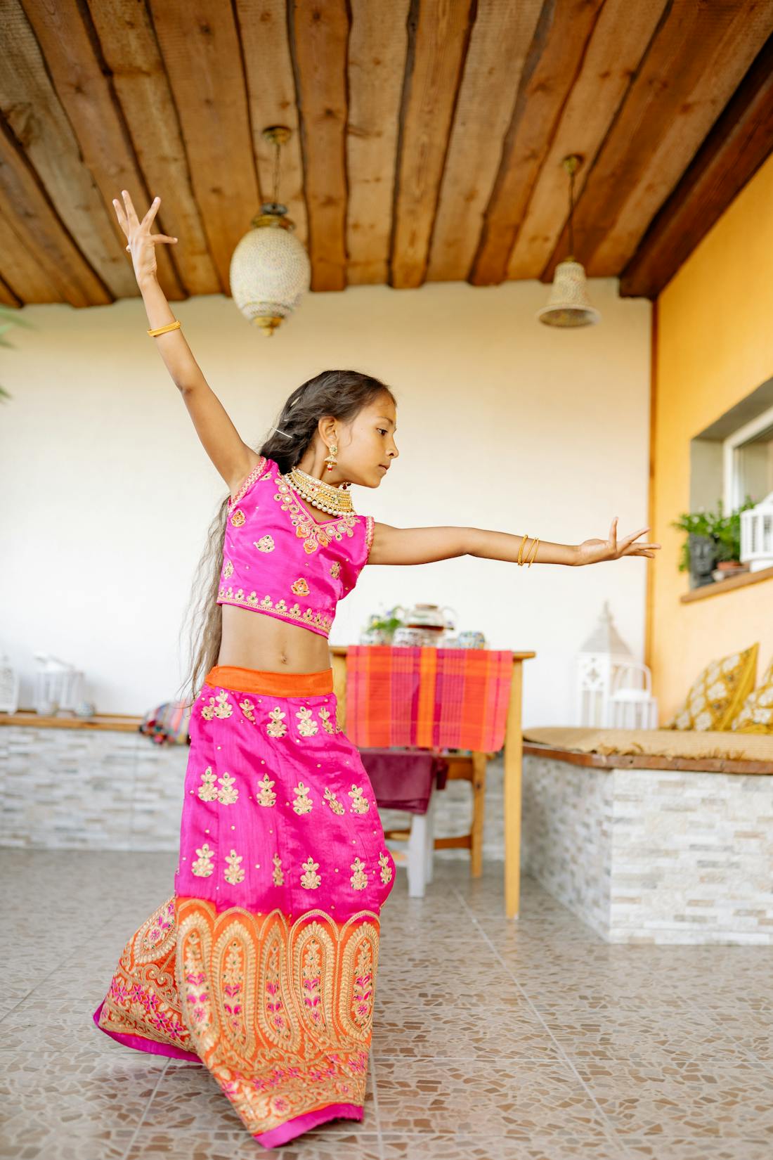 Little girl dancing indoors wearing a vibrant pink saree with pre-set pleats