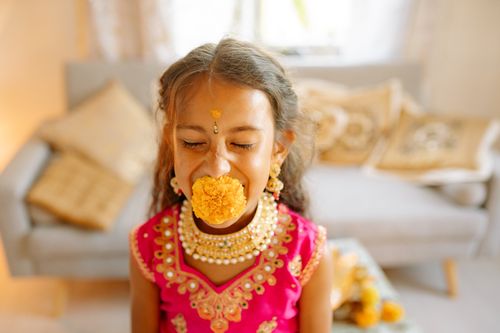 Free A young girl in traditional attire celebrates Diwali with a marigold flower indoors. Stock Photo