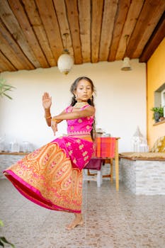 A young girl gracefully dances indoors wearing vibrant traditional Indian attire, capturing cultural essence.