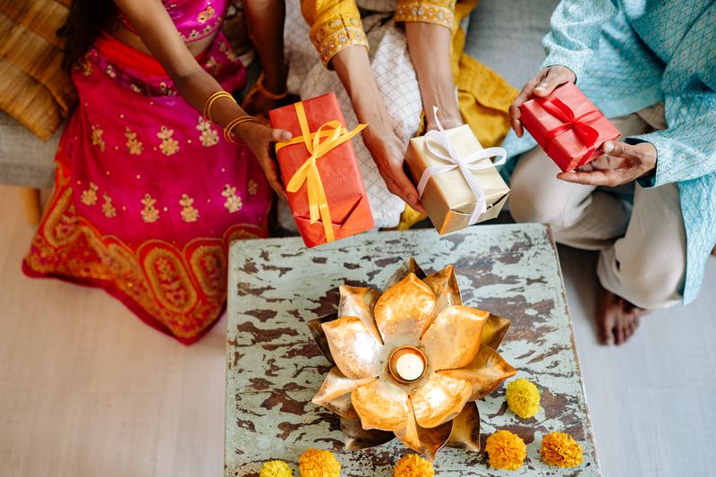 Montello festive gifting: family in traditional clothes exchanging gift boxes around a lit diya and marigolds