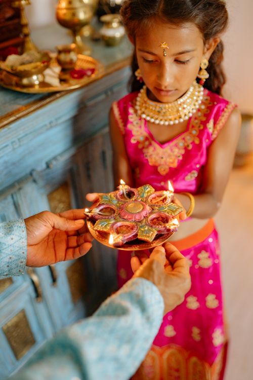 Free A young girl in traditional Indian attire participates in a vibrant Diwali celebration lighting diyas indoors. Stock Photo