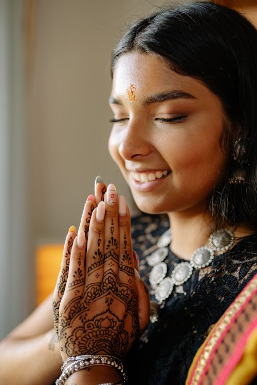 Free A young Indian woman with henna and jewelry, eyes closed and smiling, in a traditional pose. Stock Photo