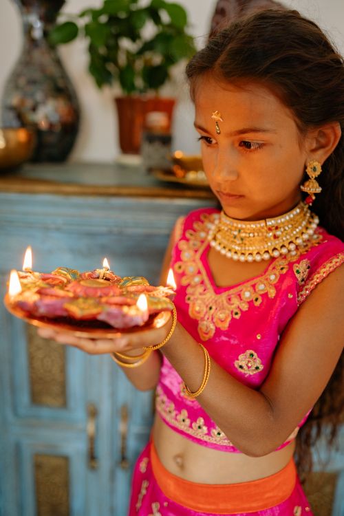 Free A young Indian girl in traditional attire holding a lit Diwali candle plate indoors. Stock Photo
