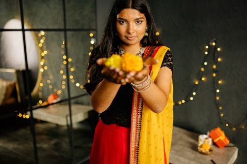 Free A woman in traditional Indian attire holding a flower offering during Diwali celebration indoors with festive lights. Stock Photo