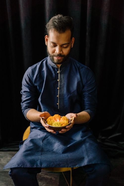 Free Man in traditional clothing holding sweets, celebrating Diwali indoors. Stock Photo