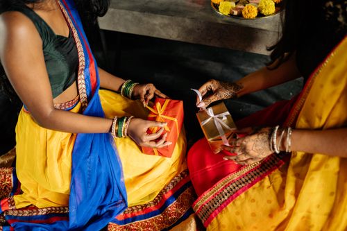 Free Women in vibrant traditional attire exchanging gifts and celebrating Diwali indoors. Stock Photo